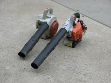 Two handheld leaf blowers sitting on a concrete driveway.