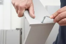 A person's hands using a small Allen wrench to tighten a screw into a white flat-pack furniture panel.