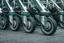 A close-up of a row of metal shopping cart caster wheels lined up on pavement outside a store.