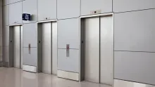 Three stainless steel elevator doors in a modern building lobby with a polished floor.