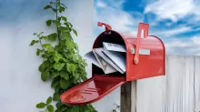 A red mailbox stuffed full of letters and envelopes with its door hanging open.