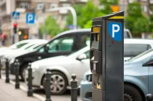 A modern parking pay station with a blue P sign in the foreground and a row of parked cars behind it on a city street.