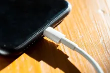 A white charging cable plugged into the bottom of a smartphone resting on a wooden table.
