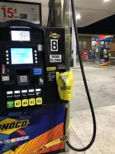 A modern gas pump at night showing its display screen, keypad and fuel grade buttons.