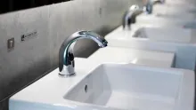 A row of white public restroom washbasins with chrome automatic sensor taps, the nearest marked number 7.