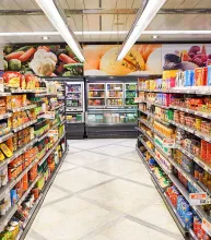 A grocery store aisle with stocked shelves on both sides and freezers at the far end.