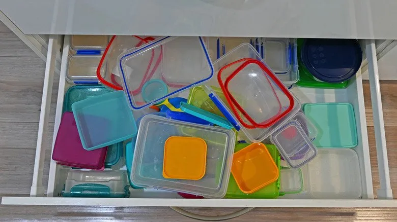A kitchen drawer overflowing with mismatched plastic food container lids in many colors and sizes.