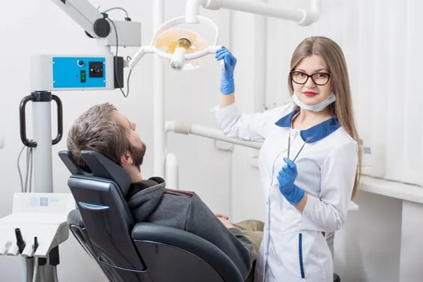 A dentist holding dental tools beside a patient reclined in a dental chair.