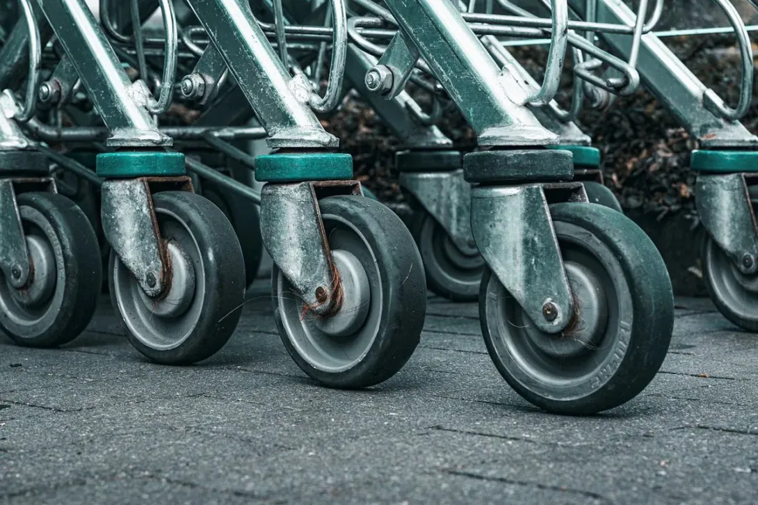 A close-up of a row of metal shopping cart caster wheels lined up on pavement outside a store.