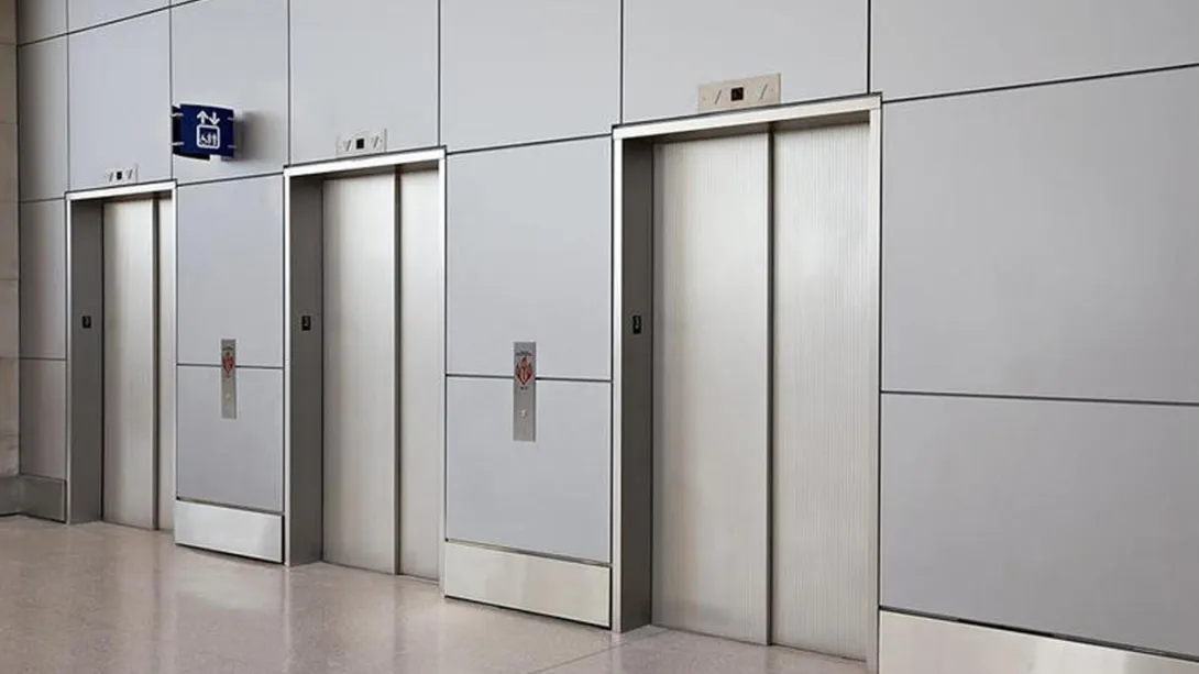 Three stainless steel elevator doors in a modern building lobby with a polished floor.