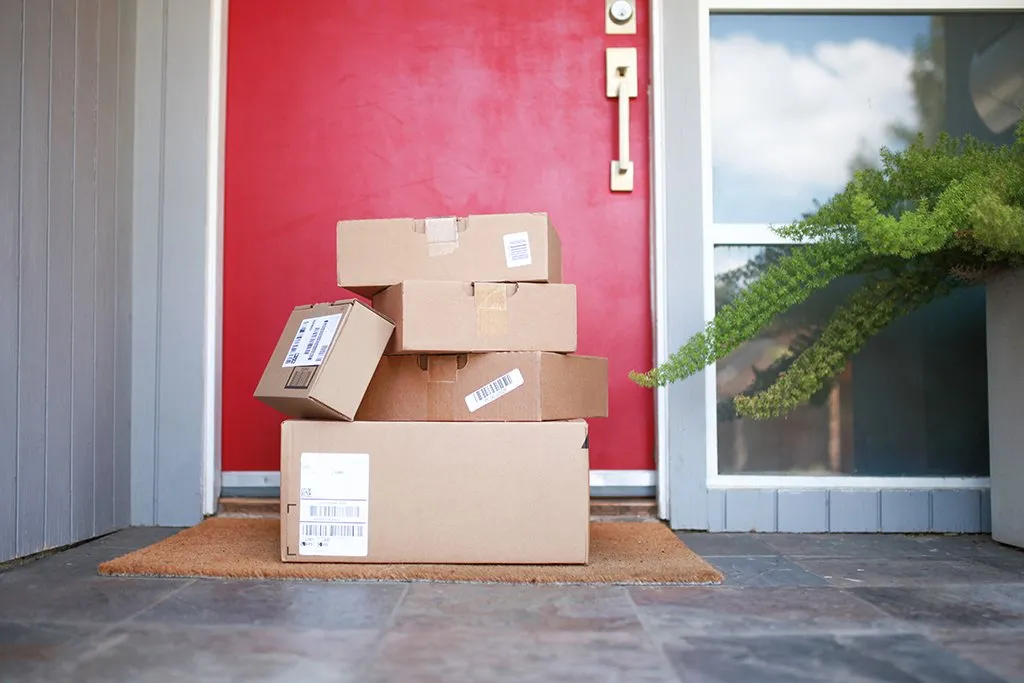 A stack of cardboard delivery packages left on a porch in front of a red front door.