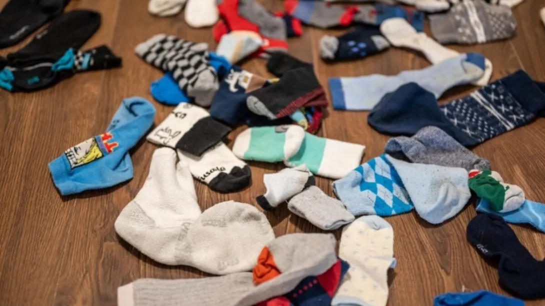 A bunch of clean unpaired socks scattered on a wooden floor, each one missing its match.