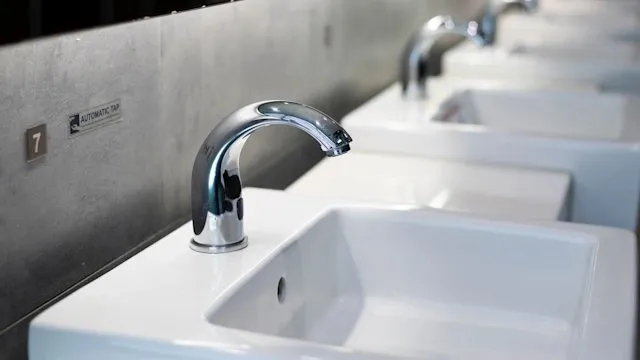 A row of white public restroom washbasins with chrome automatic sensor taps, the nearest marked number 7.