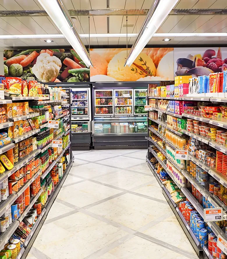 A grocery store aisle with stocked shelves on both sides and freezers at the far end.