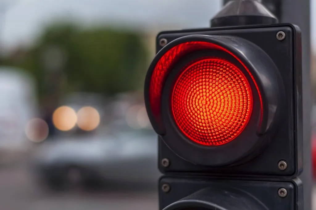 A close-up of a traffic light glowing bright red above a blurred street.