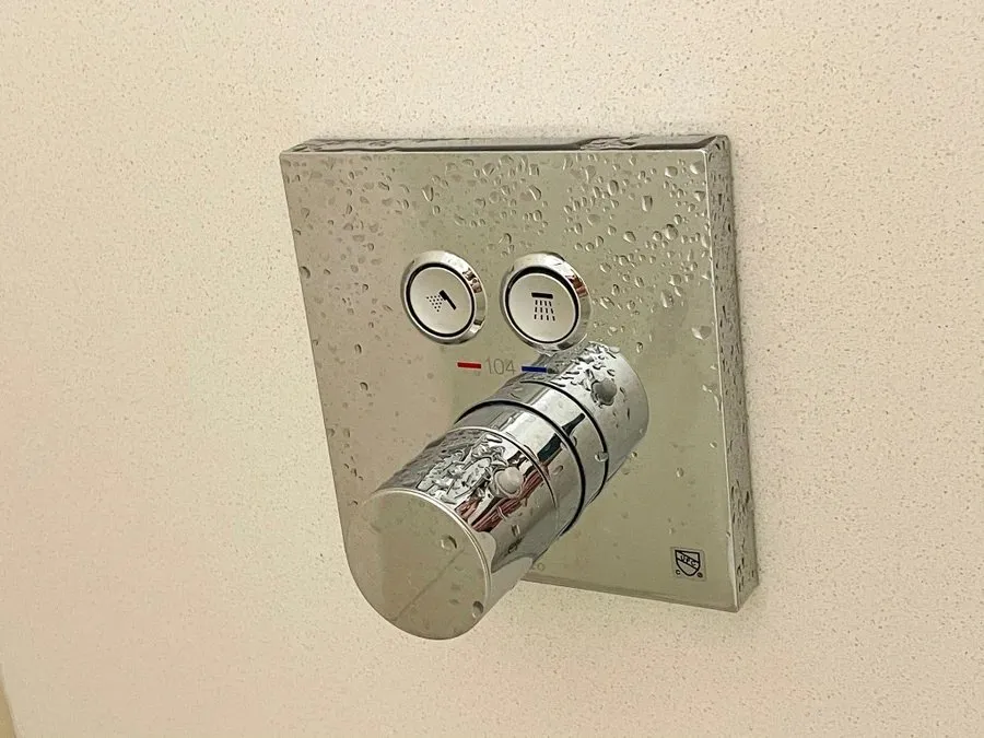 A chrome hotel shower control panel with two push buttons and a large temperature dial covered in water droplets.